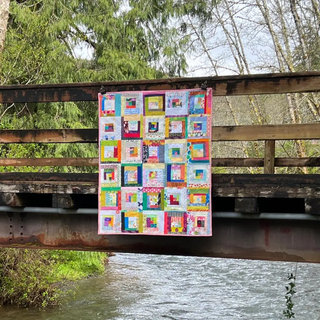 Colorful scrappy log cabin quilt hanging on rustic bridge