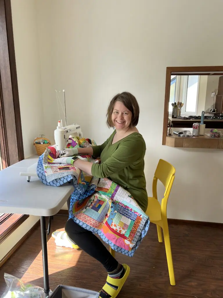 Smiling Woman Sewing Colorful Patchwork Quilt at Home in Salem
